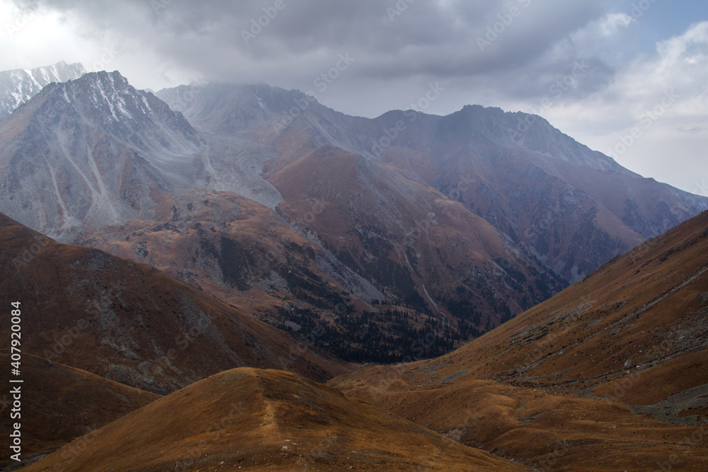 Alpine Prohodnoe gorge with rocks, hills in clouds in autumn. Mountain gorge in autumn in the fog, the slopes of the mountains are covered with yellow grass and forest, snow on rocky peaks, low clouds Alpine Prohodnoe gorge with rocks, hills in clouds in autumn. Mountain gorge in autumn in the fog, the slopes of the mountains are covered with yellow grass and forest, snow on rocky peaks, low clouds