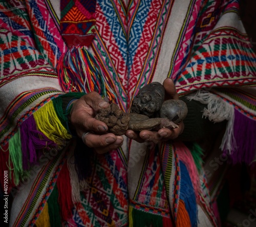 Indigenous farmer in typical traditional handwoven poncho clothes holding potatoes in hands Palccoyo village Cuzco Peru
