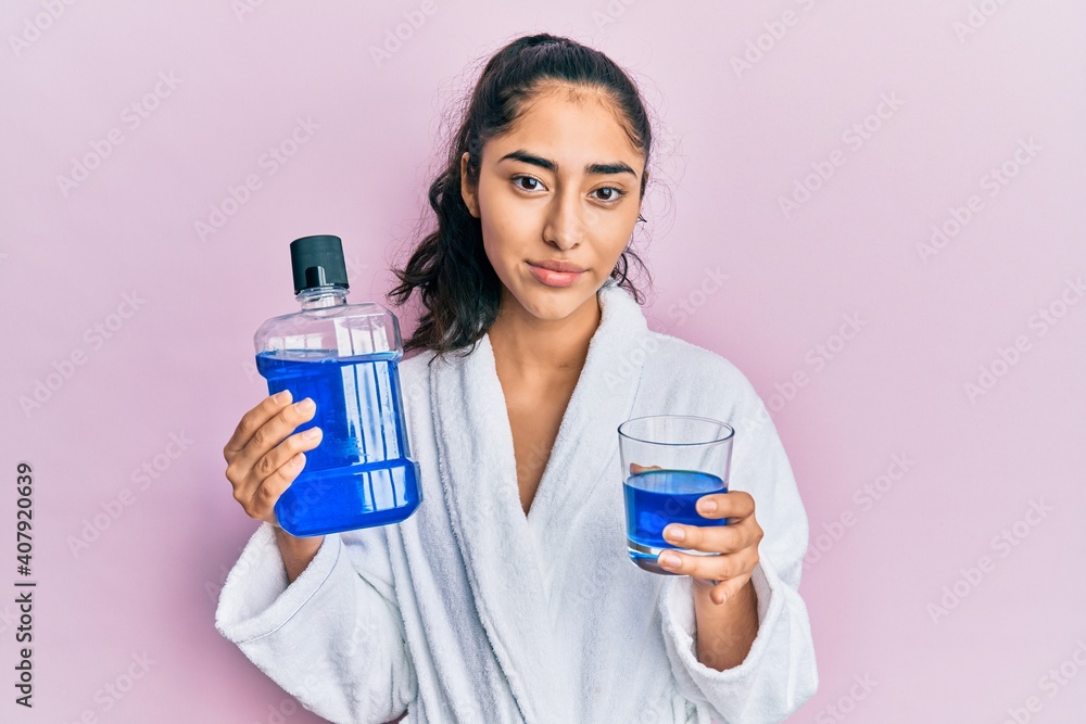 Hispanic teenager girl with dental braces holding mouthwash relaxed with serious expression on face. simple and natural looking at the camera. Hispanic teenager girl with dental braces holding mouthwash relaxed with serious expression on face. simple and natural looking at the camera.