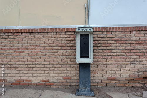 Remains of a pay telephone booth against brick wall in rural New Mexico