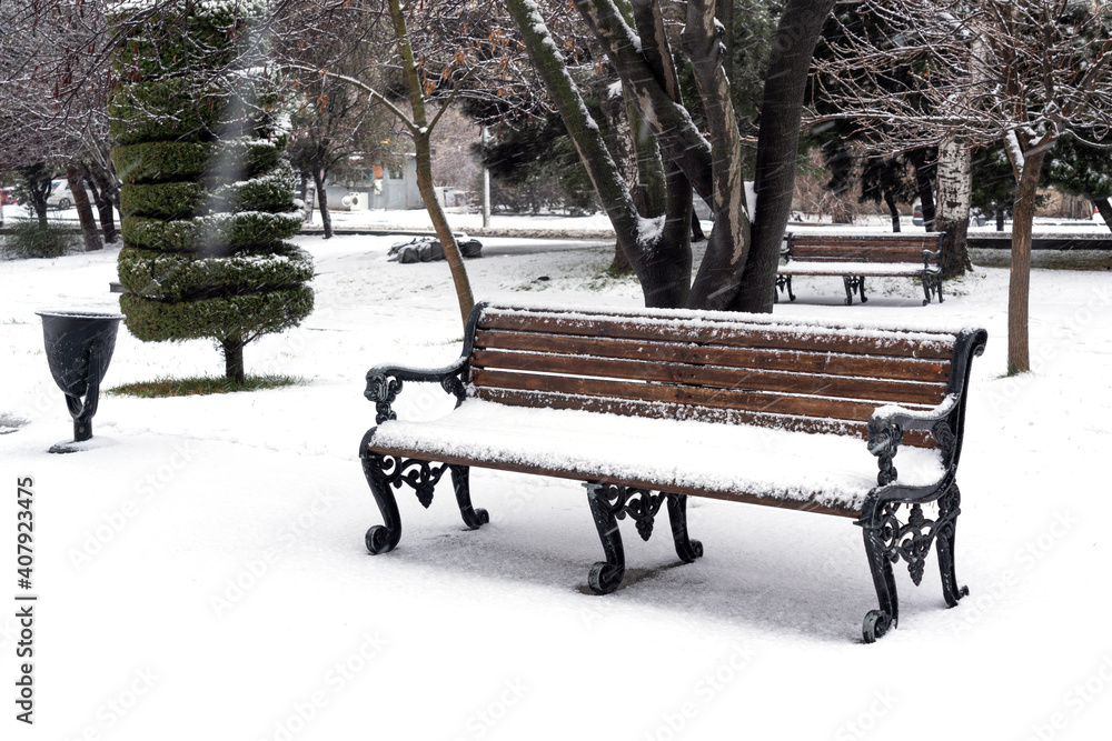 Bench in city park is covered with snow