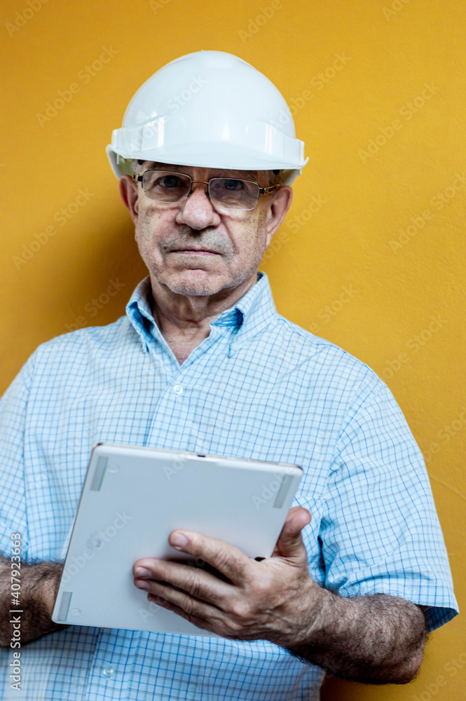 Man in a white shirt and engineer helmet holding a tablet with a yellow background.