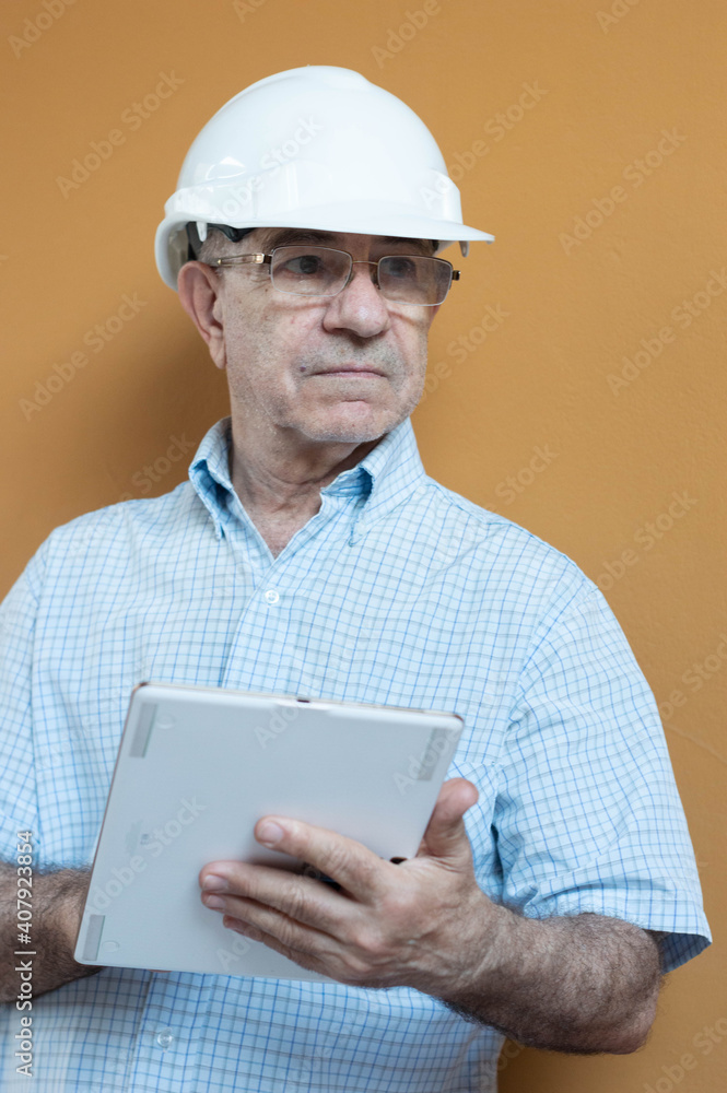Man in a white shirt and engineer helmet holding a tablet with a yellow background. Man in a white shirt and engineer helmet holding a tablet with a yellow background.
