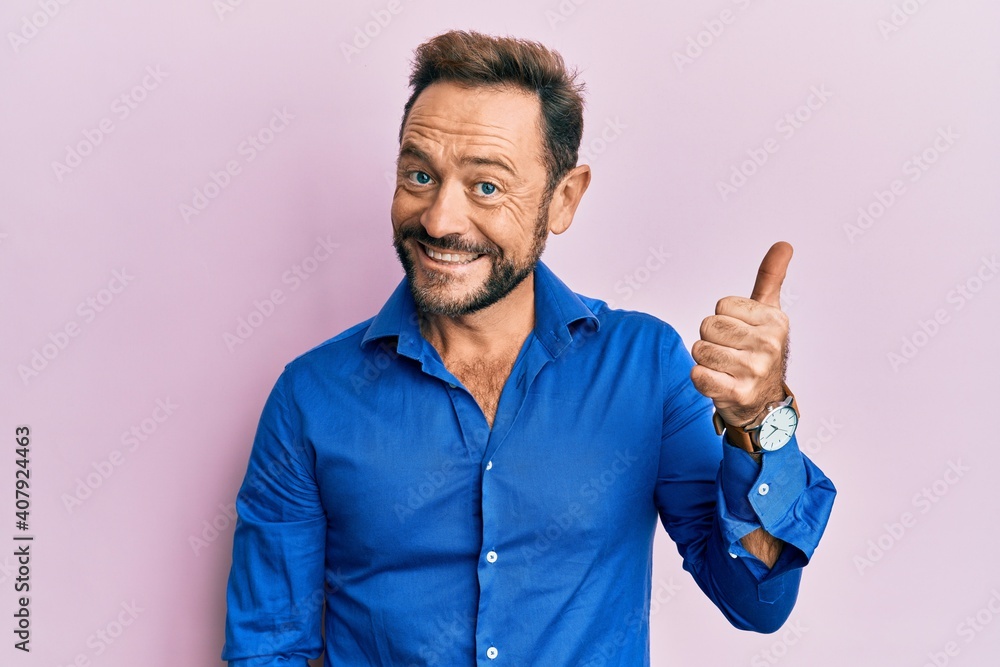 Middle age man wearing casual clothes smiling with happy face looking and pointing to the side with thumb up. Middle age man wearing casual clothes smiling with happy face looking and pointing to the side with thumb up.