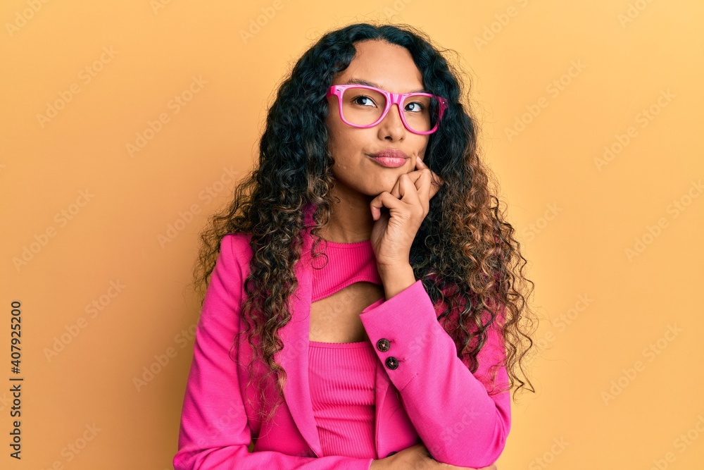 Young latin woman wearing business style and glasses thinking concentrated about doubt with finger on chin and looking up wondering Young latin woman wearing business style and glasses thinking concentrated about doubt with finger on chin and looking up wondering