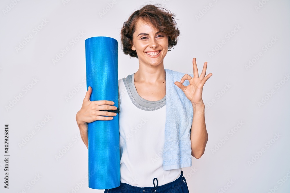 Young hispanic woman holding yoga mat doing ok sign with fingers, smiling friendly gesturing excellent symbol Young hispanic woman holding yoga mat doing ok sign with fingers, smiling friendly gesturing excellent symbol