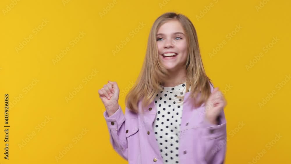 Cheerful excited happy little blonde kid girl 12-13 in violet clothes isolated on yellow background. Childhood lifestyle concept. Looking aside doing winner gesture applause cheering clapping hands Cheerful excited happy little blonde kid girl 12-13 in violet clothes isolated on yellow background. Childhood lifestyle concept. Looking aside doing winner gesture applause cheering clapping hands