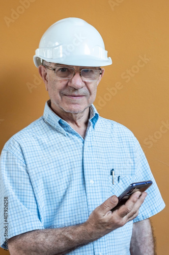 Smiling man with white engineer helmet with a mobile in his hand with yellow background