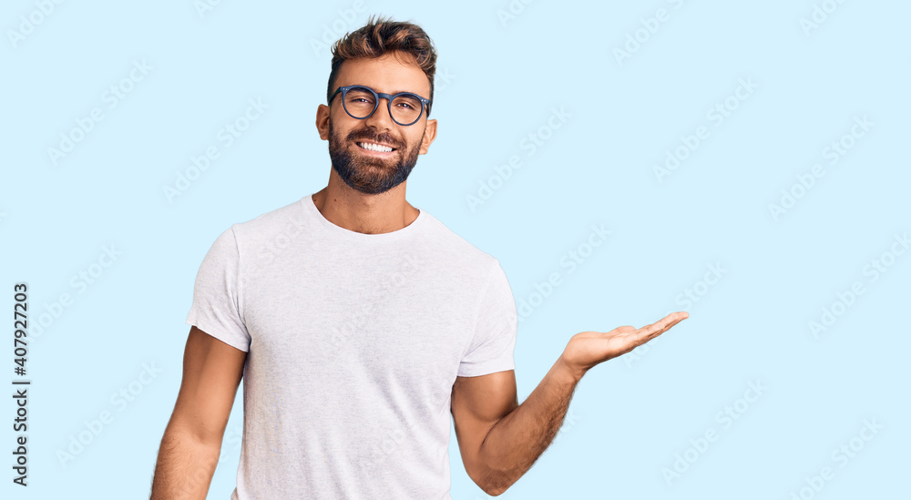 Young hispanic man wearing casual clothes and glasses smiling cheerful presenting and pointing with palm of hand looking at the camera. Young hispanic man wearing casual clothes and glasses smiling cheerful presenting and pointing with palm of hand looking at the camera.