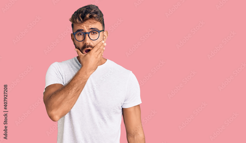Young hispanic man wearing casual clothes and glasses looking fascinated with disbelief, surprise and amazed expression with hands on chin