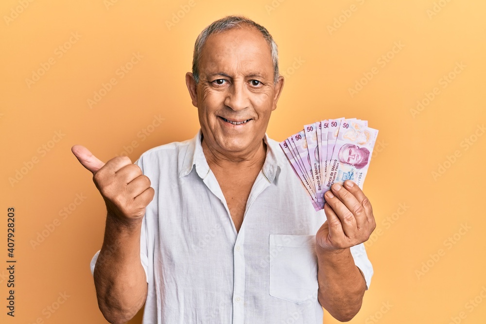 Handsome mature man holding 50 mexican pesos banknotes smiling happy and positive, thumb up doing excellent and approval sign Handsome mature man holding 50 mexican pesos banknotes smiling happy and positive, thumb up doing excellent and approval sign