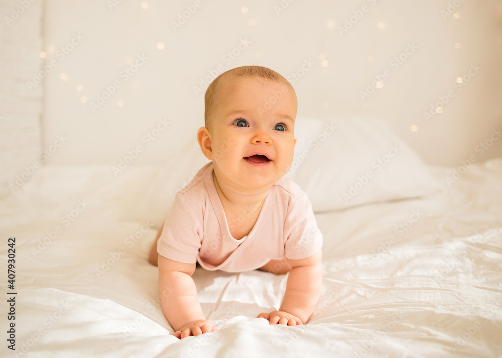 happy little baby girl in a pink bodysuit is on all fours on the bed
