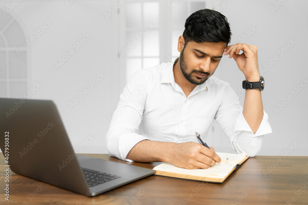 Close up photo of smart successful indian businessman ceo worker work on laptop make notes in copybook Close up photo of smart successful indian businessman ceo worker work on laptop make notes in copybook