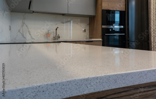 White kitchen countertop, marble backsplash, gray kitchen cabinets, black kitchen appliances. Metal tap and liquid soap dispenser.