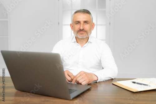 Middle age handsome businessman wearing tie sitting using laptop at the office with serious expression on face