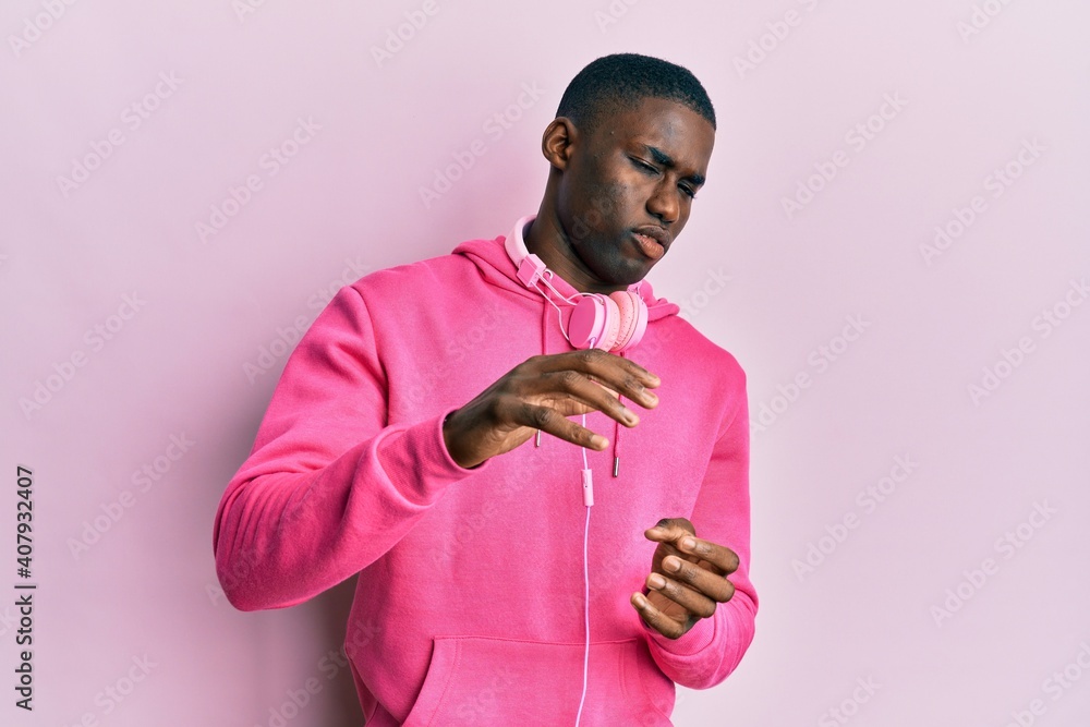 Young african american man wearing gym clothes and using headphones disgusted expression, displeased and fearful doing disgust face because aversion reaction. with hands raised Young african american man wearing gym clothes and using headphones disgusted expression, displeased and fearful doing disgust face because aversion reaction. with hands raised