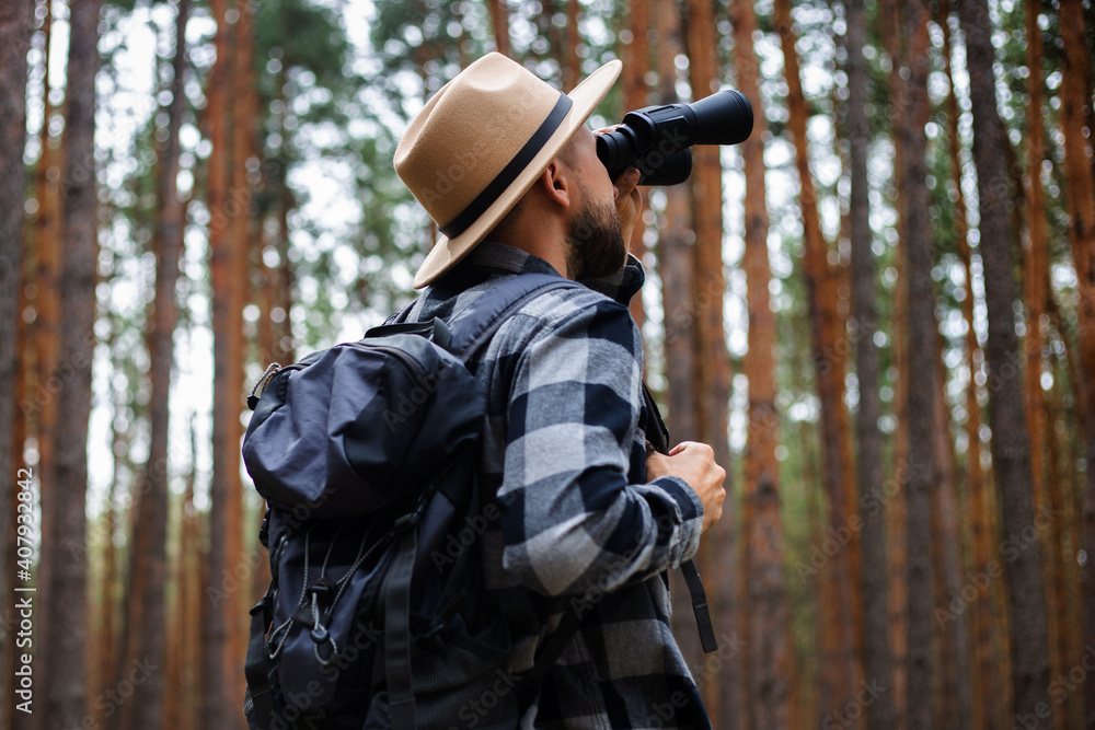 Male tourist looking through binoculars in the forest