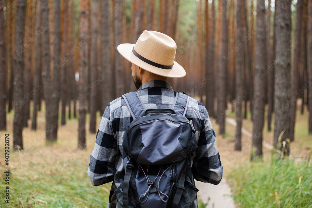 Man in a hat and a plaid shirt holds binoculars and walks through the forest