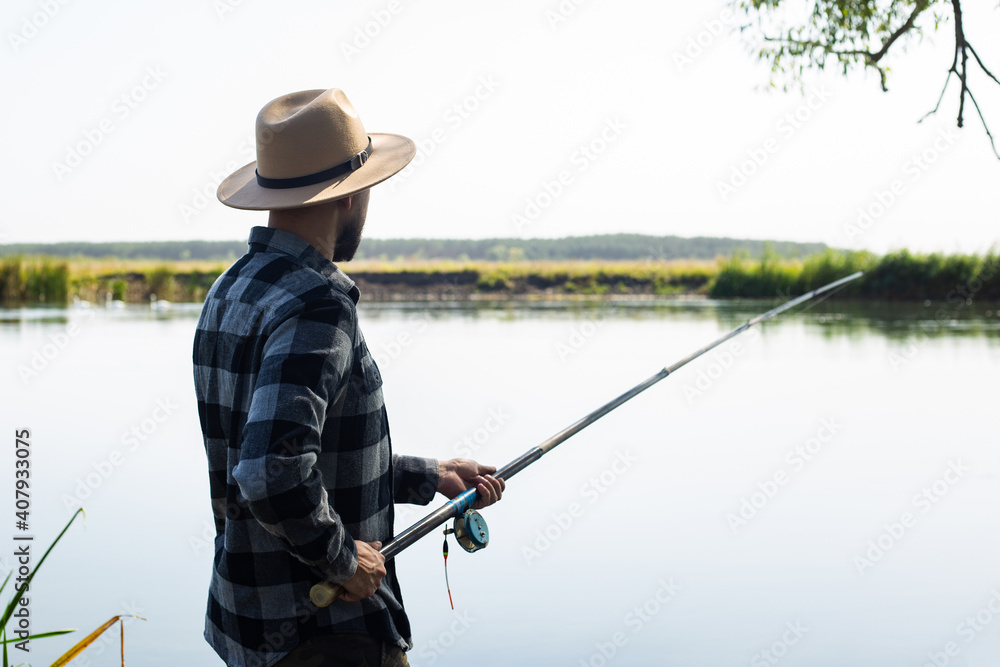 Man in a hat and a plaid shirt is fishing on a line by the river Man in a hat and a plaid shirt is fishing on a line by the river