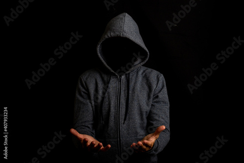 Man without a face in a hood holds something in his hands on a dark background