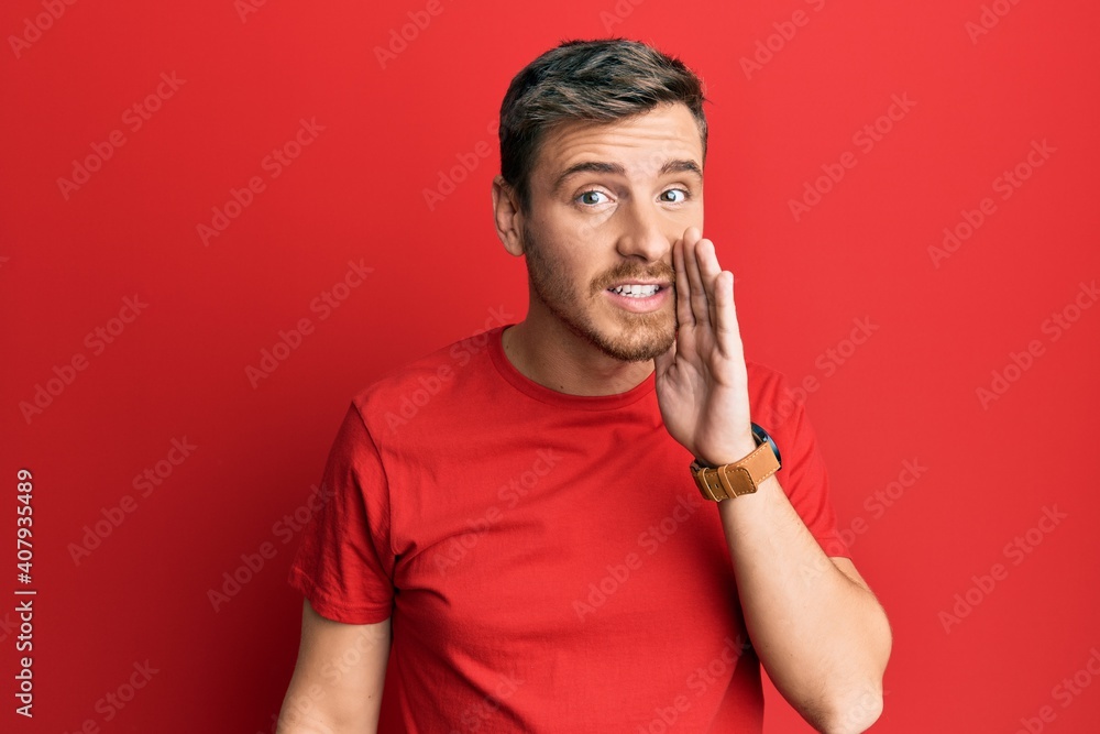 Handsome caucasian man wearing casual red tshirt hand on mouth telling secret rumor, whispering malicious talk conversation Handsome caucasian man wearing casual red tshirt hand on mouth telling secret rumor, whispering malicious talk conversation