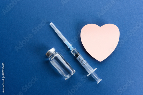 Medical ampoules with a vaccine and a sticker in the form of a heart on a blue background.
