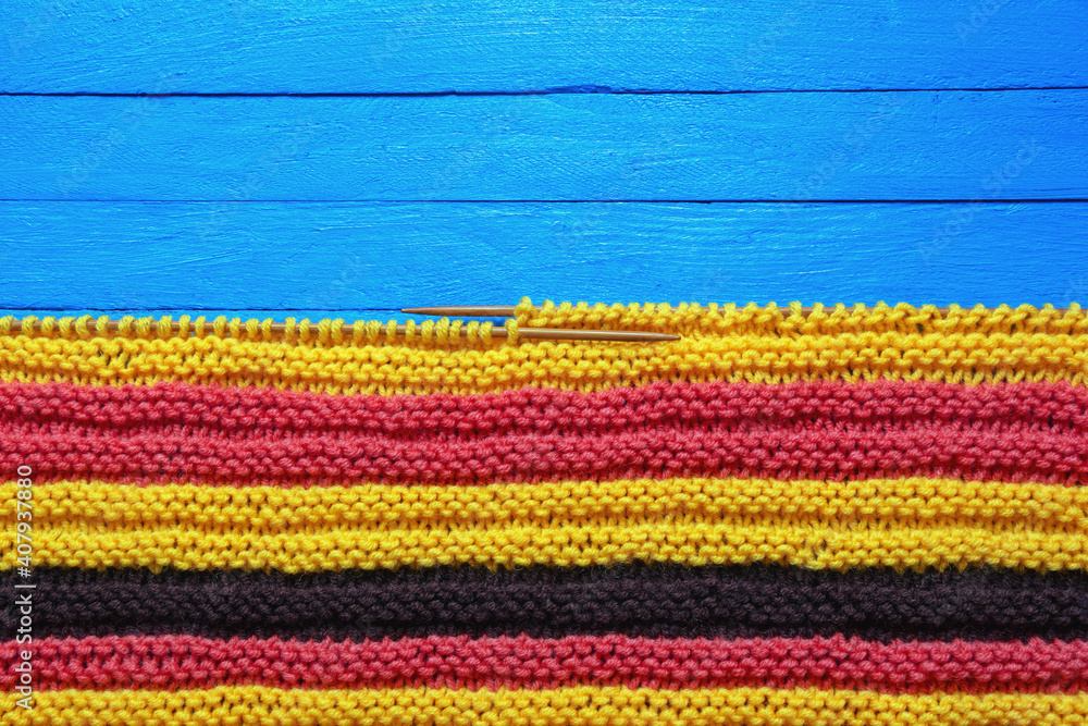 Hobbies and knitting concepts. Bright striped knitted cloth with knitting needles on  blue rustic table. Copy space
