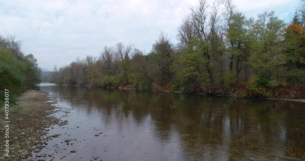 Low drone flying over pristine Sava river in Slovenia. Reflection of trees growing on river bank in calm blue water. Right pan