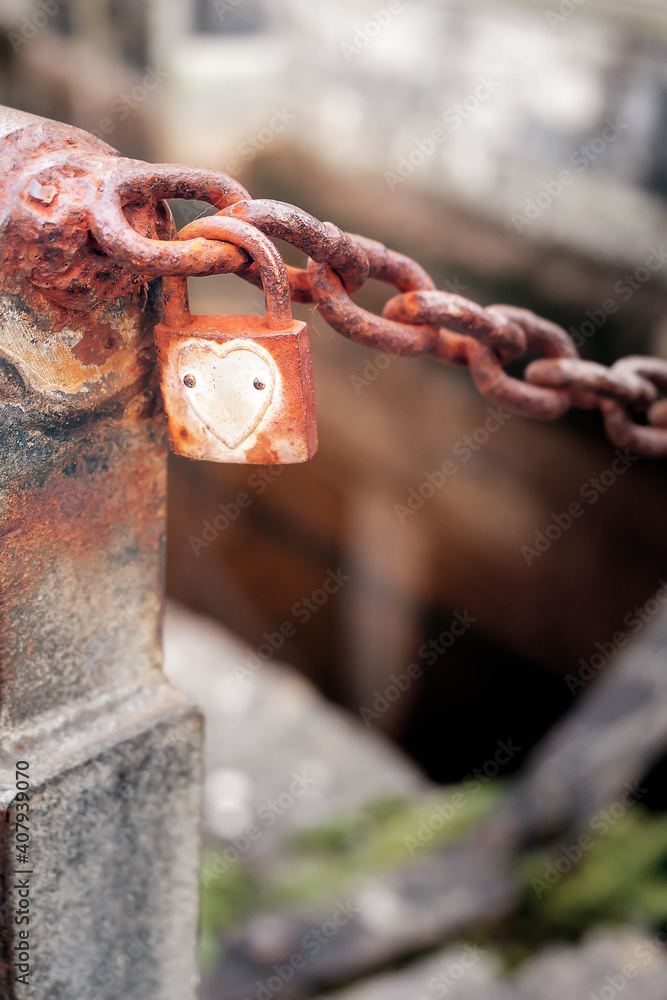Old rusty padlock with heart shape on a metal chain, selective focus. Town folklore and legend concept. Old rusty padlock with heart shape on a metal chain, selective focus. Town folklore and legend concept.