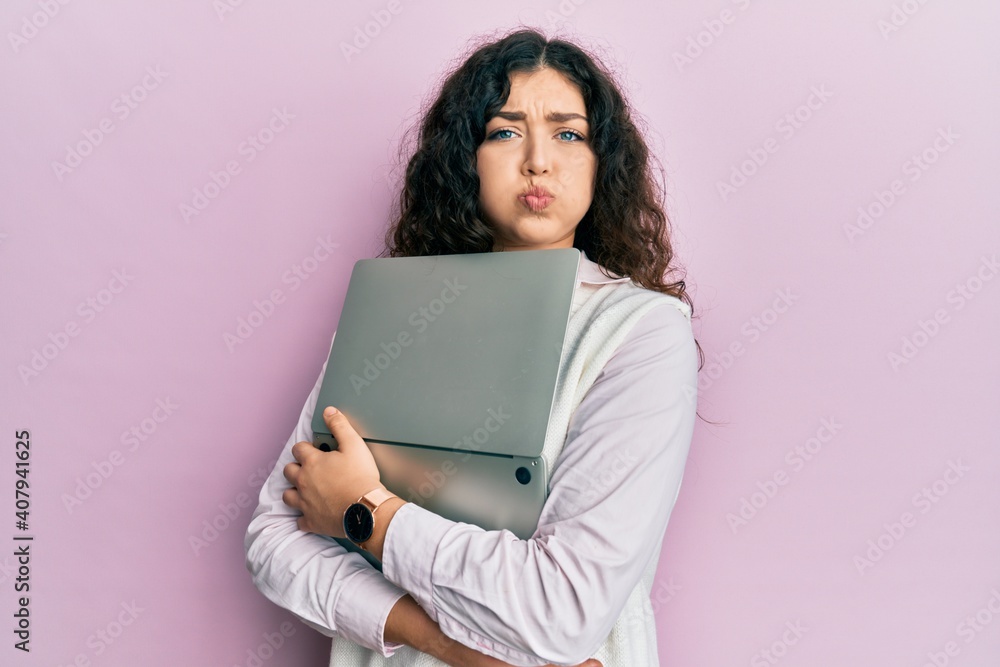 Young brunette woman with curly hair hugging laptop with love puffing cheeks with funny face. mouth inflated with air, catching air. Young brunette woman with curly hair hugging laptop with love puffing cheeks with funny face. mouth inflated with air, catching air.