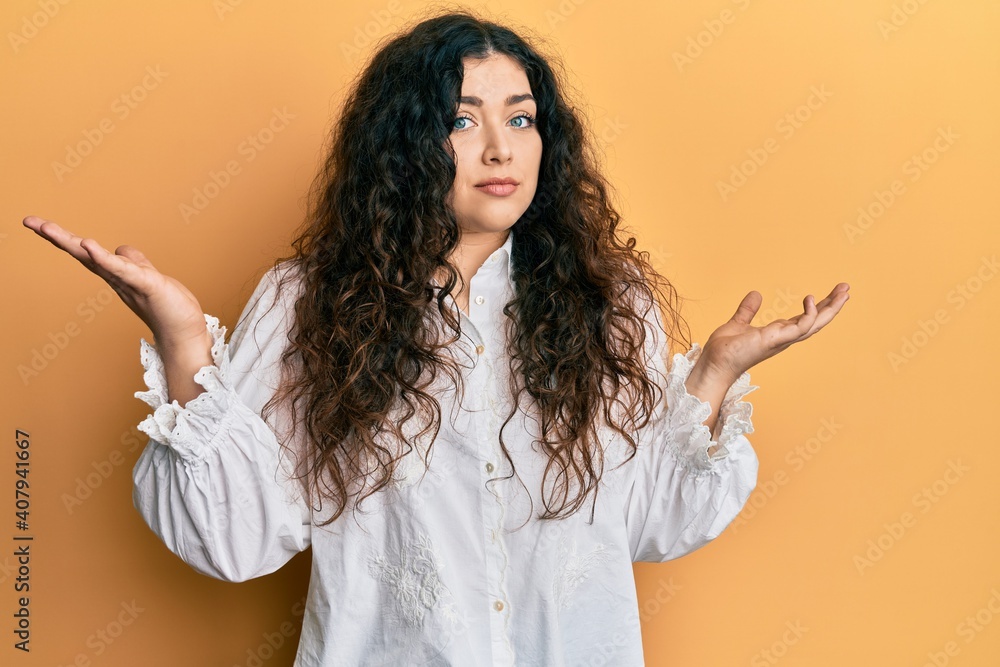 Young brunette woman with curly hair wearing casual clothes clueless and confused with open arms, no idea and doubtful face. Young brunette woman with curly hair wearing casual clothes clueless and confused with open arms, no idea and doubtful face.