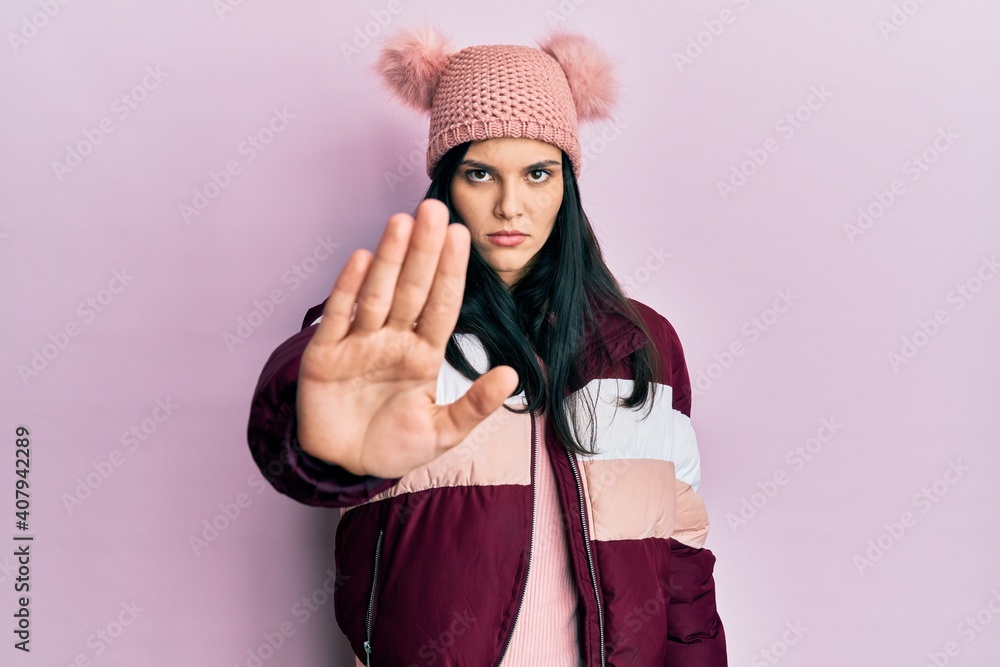 Young hispanic woman wearing wool winter sweater and cap doing stop sing with palm of the hand. warning expression with negative and serious gesture on the face. Young hispanic woman wearing wool winter sweater and cap doing stop sing with palm of the hand. warning expression with negative and serious gesture on the face.