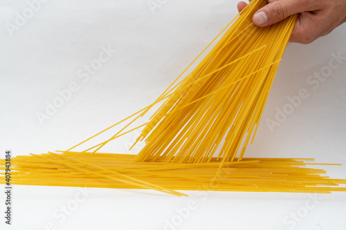 Closeup shot of a hand poruing dry spaghetti on a wh photo