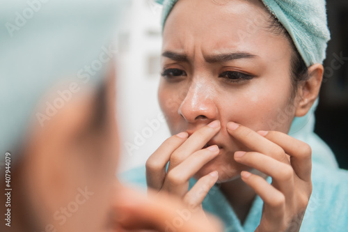 Obraz na plátne close up of asian girl squeezing pimple on the cheek to the mirror with towel on