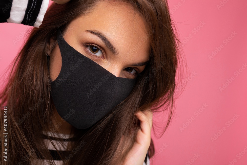 Closeup photo of young beautiful woman in reusable virus protective mask on face against coronavirus isolated on the pink background wall Closeup photo of young beautiful woman in reusable virus protective mask on face against coronavirus isolated on the pink background wall