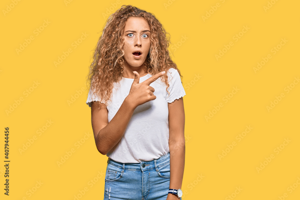 Beautiful caucasian teenager girl wearing casual white tshirt surprised pointing with finger to the side, open mouth amazed expression. Beautiful caucasian teenager girl wearing casual white tshirt surprised pointing with finger to the side, open mouth amazed expression.