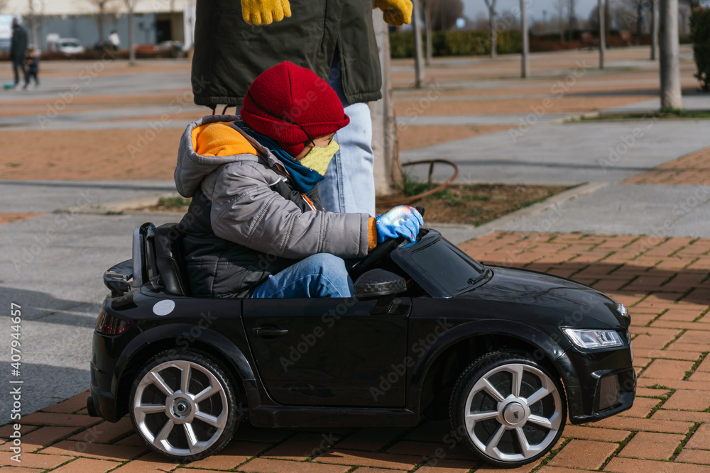 child driving a toy car down the street wearing a hat, earmuffs and a scarf, and wearing a cold weather jacket child driving a toy car down the street wearing a hat, earmuffs and a scarf, and wearing a cold weather jacket