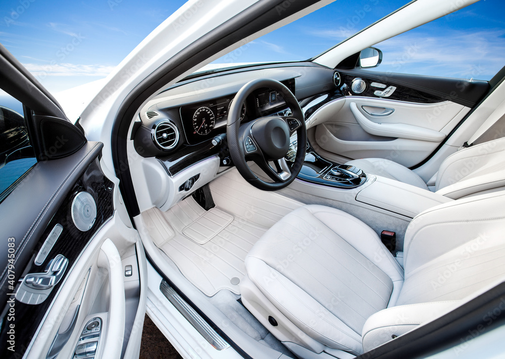 The car is inside. The interior of a prestigious modern car. Front seats with steering wheel, dashboard and display. white leather interior with black dashboard. on sky background