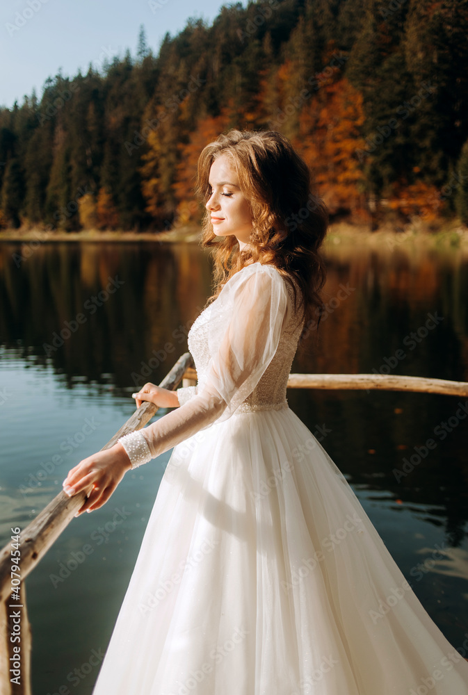A beautiful bride in a luxurious wedding dress enjoys the views of a mountain lake A beautiful bride in a luxurious wedding dress enjoys the views of a mountain lake