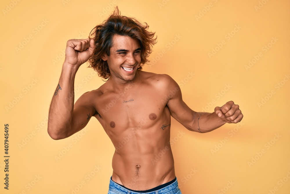 Young hispanic man standing shirtless dancing happy and cheerful, smiling moving casual and confident listening to music Young hispanic man standing shirtless dancing happy and cheerful, smiling moving casual and confident listening to music