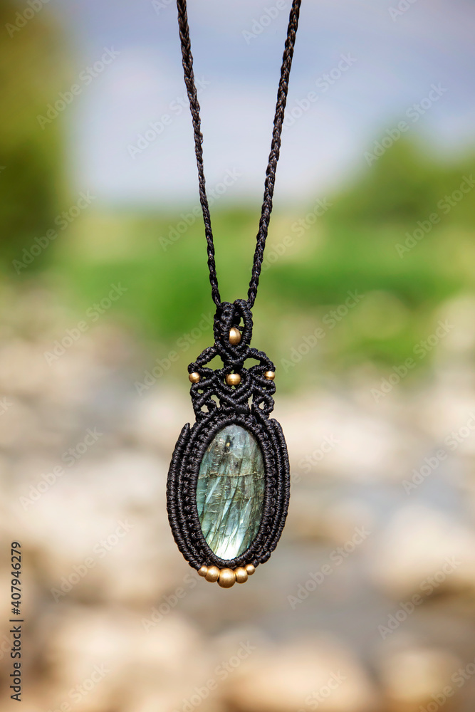 Beautiful necklace in boho style with labradorite mineral stone on natural blury landscape background Beautiful necklace in boho style with labradorite mineral stone on natural blury landscape background
