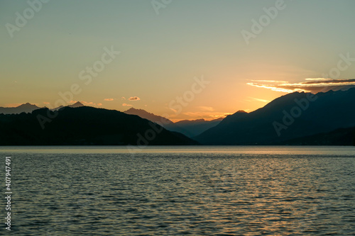 A sunset by Millstaetter lake in Austria. The lake is surrounded by high Alps. Calm surface of the lake reflecting the sunbeams. The sun sets behind the mountains. A bit of overcast. Natural beauty