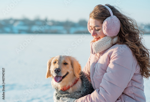 Smiling woman with long curls hugs her pet dog golden retriever near face. Golden retriever smiling with a woman walking outdoors winter day, warm clothing. love and care for the pet. © trofalena