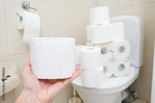 Many toilet paper rolls at home of hoarder, buying too much of hygienic means during pandemia, a hand holding a roll of toilet paper in a bathroom