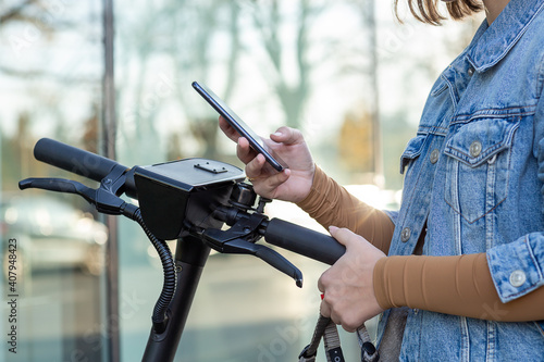 Studentin in Jeans Jacke bezahlt mit Smartphone für E Scooter