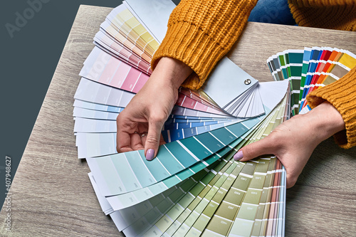 Color wheel for choosing paint tone. Hands of female interior designer working with palette for choosing colors. Creative process concept. Comparing options with matching hues.