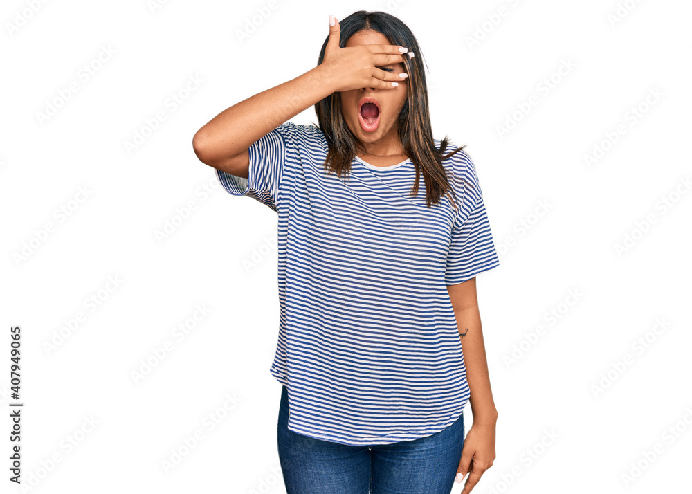 Young latin girl wearing casual clothes peeking in shock covering face and eyes with hand, looking through fingers with embarrassed expression. Young latin girl wearing casual clothes peeking in shock covering face and eyes with hand, looking through fingers with embarrassed expression.