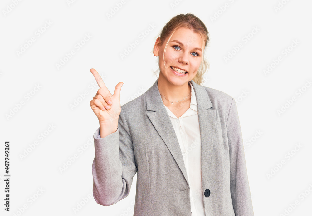 Young beautiful blonde woman wearing elegant jacket pointing finger up with successful idea. exited and happy. number one. Young beautiful blonde woman wearing elegant jacket pointing finger up with successful idea. exited and happy. number one.