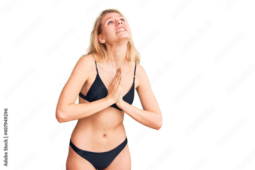 Young beautiful blonde woman wearing bikini begging and praying with hands together with hope expression on face very emotional and worried. begging. Young beautiful blonde woman wearing bikini begging and praying with hands together with hope expression on face very emotional and worried. begging.