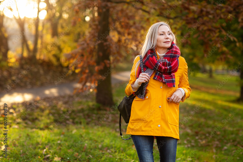 Weißhaarige Grauhaarige Frau spaziert im Park Herbst Sonnenstrahlen gelbe Regenmantel Weißhaarige Grauhaarige Frau spaziert im Park Herbst Sonnenstrahlen gelbe Regenmantel